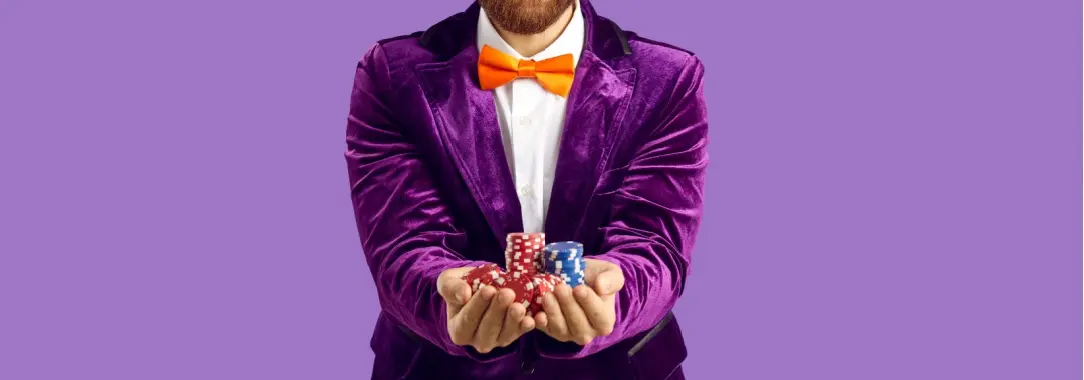 smiling man with short beard dressed in purple suit and hat with orange bow tie holding poker chips