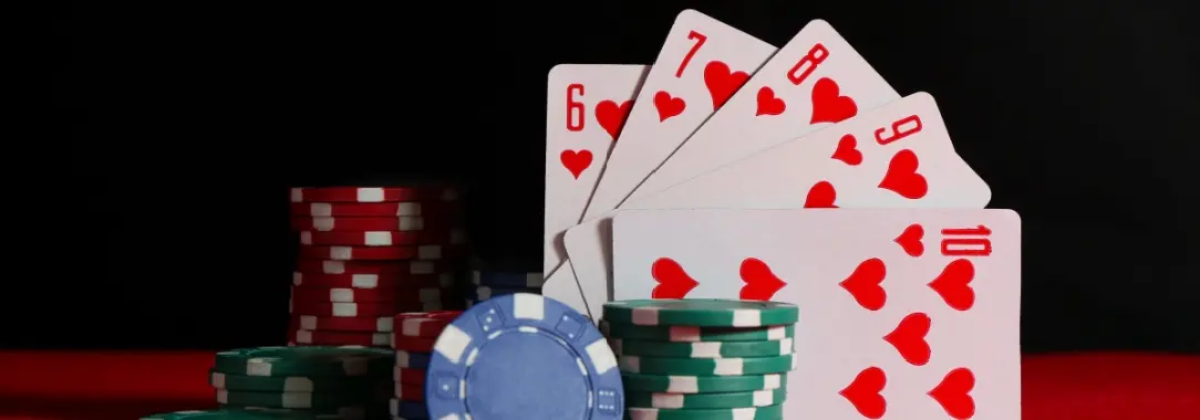 a poker hand of a straight flush in hearts leaning against poker chips of various colors