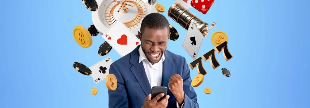 A photo of a happy guy surrounded by gaming paraphernalia holding a smart phone in one hand and clenching the other 