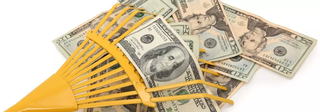 A photo of a yellow rake raking in piles of dollar bills isolated on a white background 