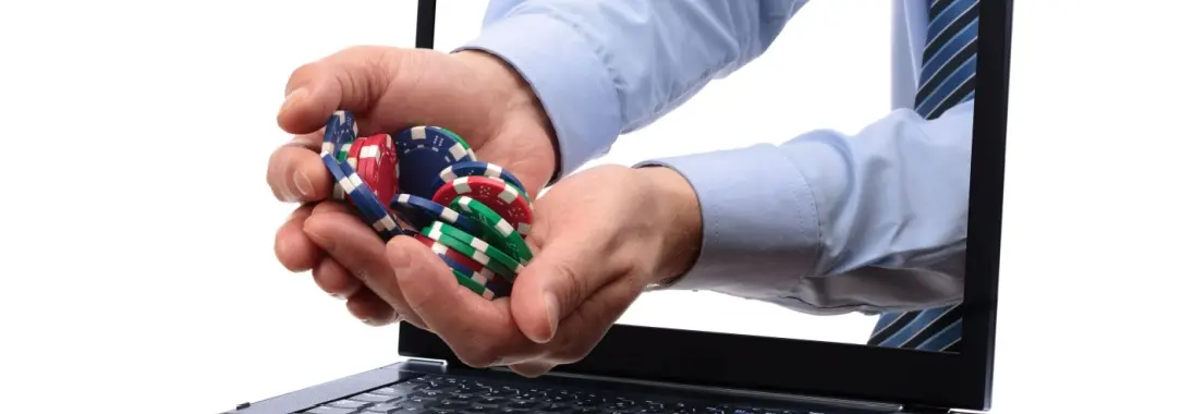 a man's hands filled with casino chips reaching out of a laptop computer screen 