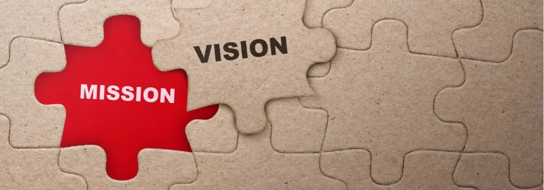 A photo of a plain cardboard jigsaw puzzle with one piece removed and the words ‘vision’ and ‘mission’ 